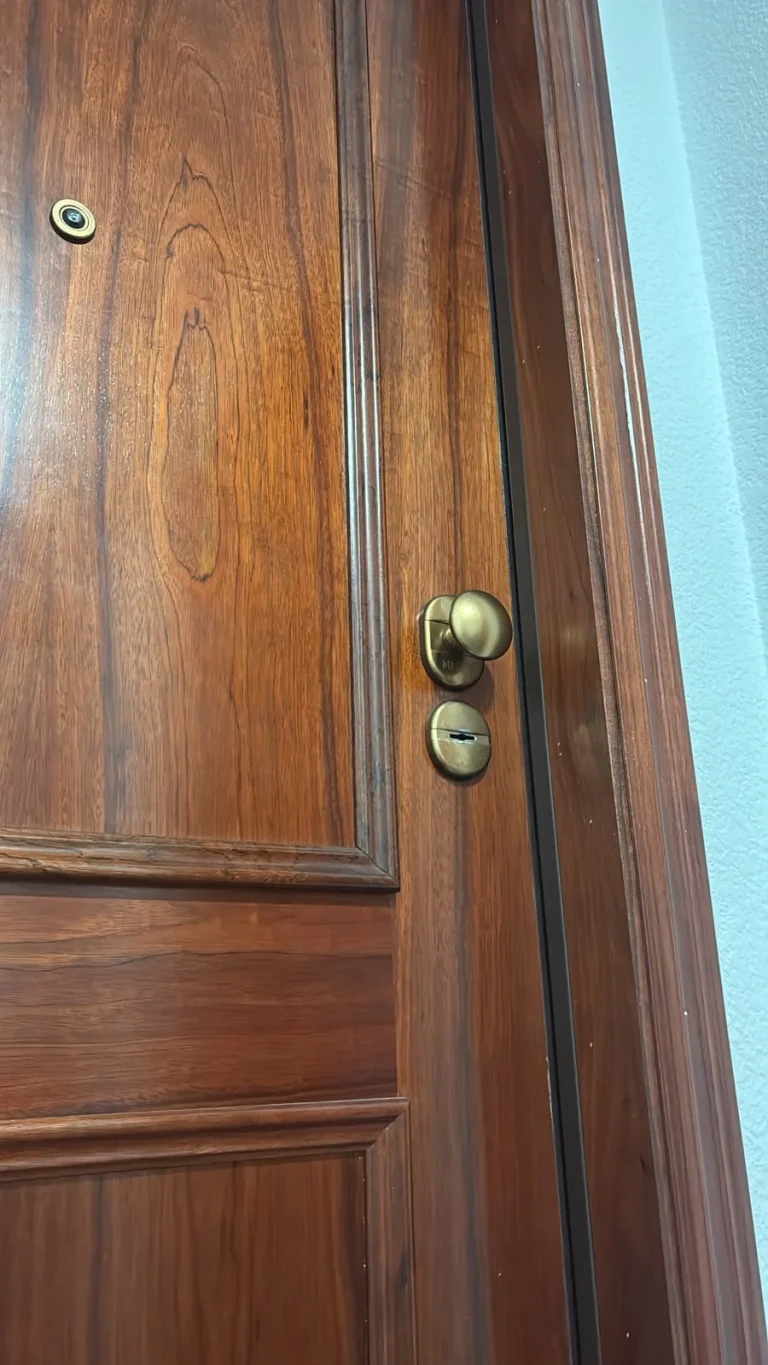 Puerta de madera de una vivienda con manivela de latón, bombín y mirilla